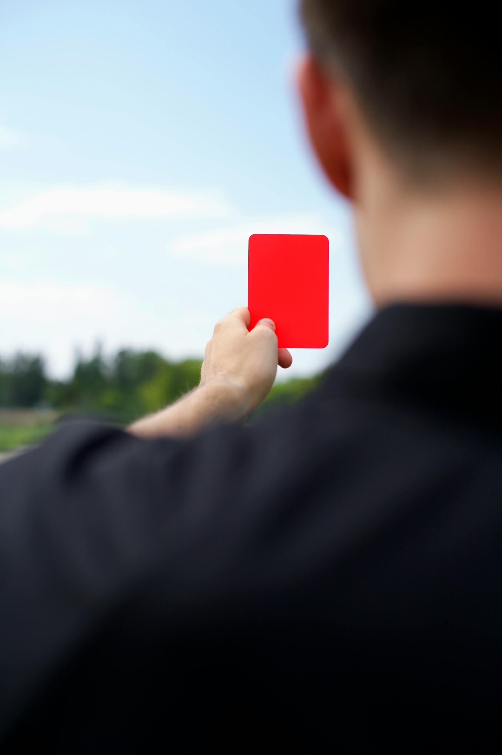 Rear view of a referee holding up a red card during a soccer match outdoors.